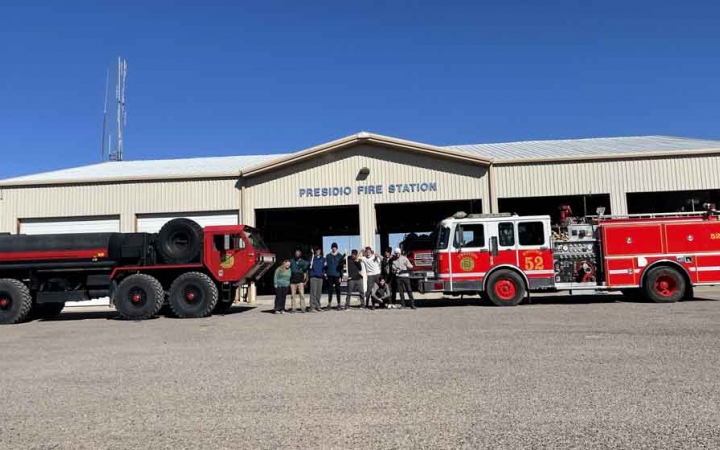 a group of students pose with fire trucks in front of a fire station after doing a service project with outward bound